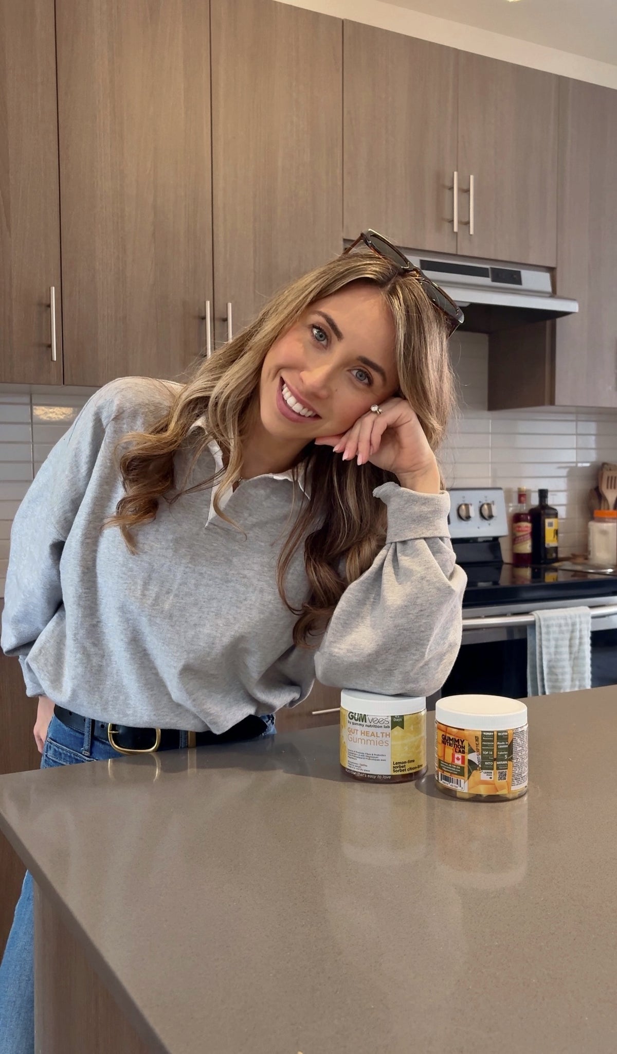 A smiling woman at her kitchen counter beside two jars of GUMvees gummies