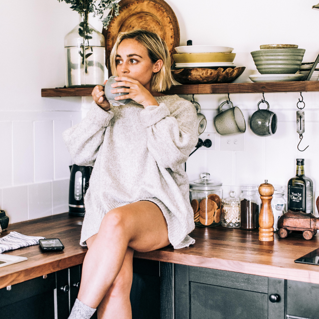 a woman sits on her kitchen counter drinking a cup of tea